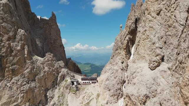 Backwards reveal drone shot of the iconic Toni Demetz Hut perched dramatically in the Forcella del Sassolungo, Dolomites, Italy