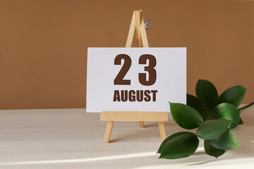 August 23th. Day 23 of month, Calendar date. Green branch, easel with the date and month on desktop. Close-up, brown background. Summer month, day of year concept