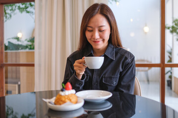 Portrait image of a woman drinking coffee with a piece of cake on the table in cafe
