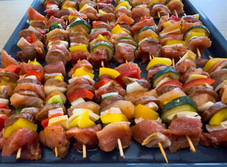 Raw skewers prepared for baking, arranged on a tray with pork, chicken, bell peppers, onions,...