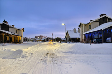 Winter evening in cottage village. The street is covered with snow. The houses are decorated with New Year's garlands with lights.