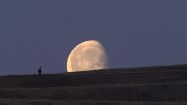Silhouette of running man on a mountain slope against large moon and night sky 