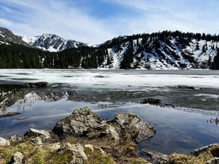 Scenic mountain lake with snowy peaks, evergreen forest, and icy reflections in spring