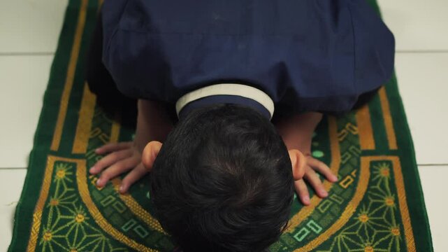 a boy is prostrating on a prayer mat, performing prayers or prayers to his god, devotion to god