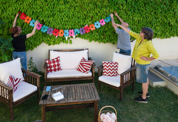 Middle-aged friends hanging colorful floral garland to decorate backyard for outdoor celebration
