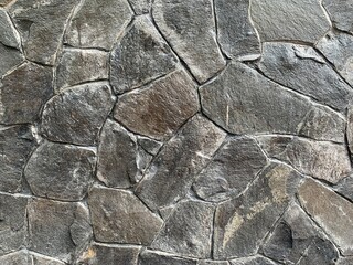 Texture of a natural stone wall constructed with irregularly shaped slate rocks in earthy tones