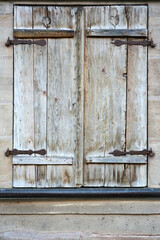 Vintage wooden shutters with heart-shaped cutouts and rusty hinges on a stone wall. Timeworn charm and history captured in every detail
