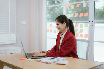 Asian businesswoman working on laptop while sitting at desk in home office.