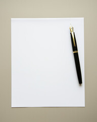 A white sheet of paper on the table with a black fountain pen next to it, top view, flat lay.