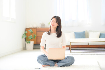 Obraz premium ノートパソコンを膝にのせて床にあぐらで座る女性の穏やかなリモートワークシーン