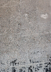Exposed concrete surface with a clearly rough, irregular texture. The structure shows porous inclusions, fine cracks, shuttering board impressions and irregular shadows through the grainy surface.