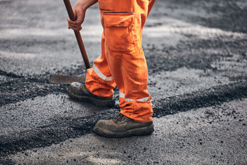 Construction worker working on a new asphalt layer on a public street.