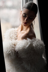 Attractive young woman wrapped in fur coat,Portrait of sensual woman, near window