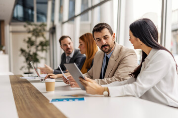 Two executives discussing data on tablet while sitting on a meeting at boardroom.