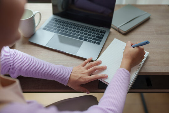 Woman writing notes in notebook while working at home office desk