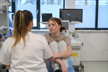 Scared teenage girl sitting on hospital bed, talking with caring doctor.