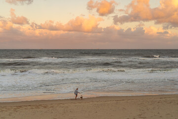 People walk their dog along the beach