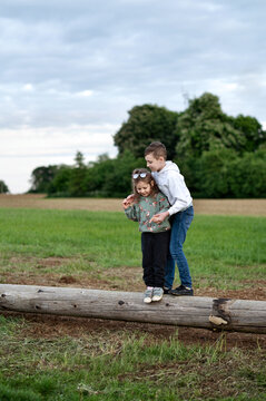 Siblings helping each other to stand on a log.
