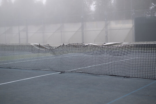 damaged tennis net on blue court in dense murky fog