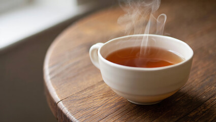 A steaming cup of tea rests on a rustic wooden table, with delicate wisps of steam rising, creating a cozy and inviting atmosphere.