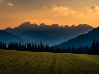 Stunning sunset over mountainous landscape with silhouette of peaks and lush green foreground.