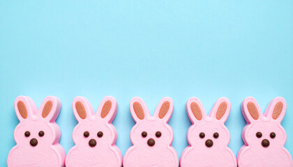 Fototapeta premium Pink bunny-shaped marshmallows lined up against a light blue background create a playful, festive atmosphere