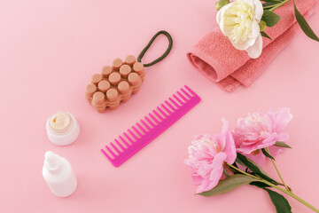 Towel with body care products and peony flowers on the pink background.