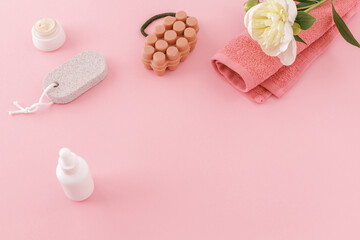 Towel with body care products and a peony flower on the pink background.