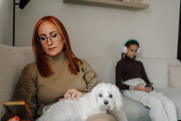 Mother petting dog while using smartphone and teenage daughter listening music with headphones