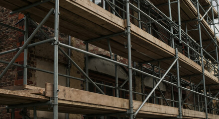 Metal scaffolding supporting brick building under renovation with wooden planks for worker access. Construction infrastructure enabling safe building restoration and facade improvement projects