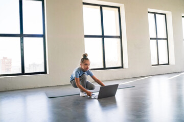 A child is performing a mountain climber exercise on a mat at home, following an online workout on her laptop