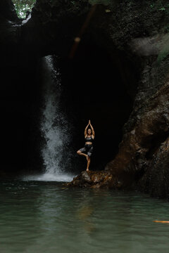 Woman practising yoga in front of waterfall on the island of Bali