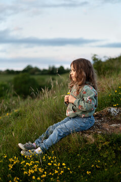 A girl sitting on slope holding a small yellow flower in her hand