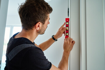 Professional handyman using spirit level to check vertical alignment of interior door during installation. Home repair and renovation