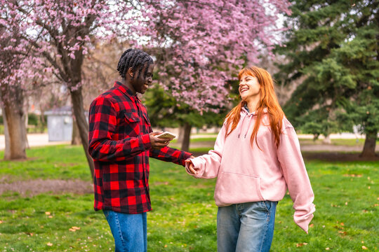 Young couple holding hands and using smartphone in spring park