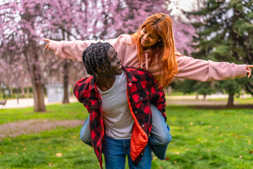 Young man giving piggyback ride to his girlfriend in spring blossom park