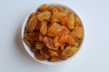 Raisins in a small white bowl, isolated on white background, flat lay or top view
