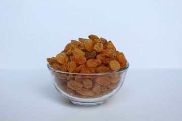 Yellow raisins in a transparent bowl, isolated on white background
