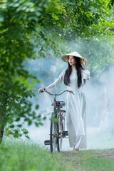 Vietnamese girl in national costume with bicycle in countryside. Ao dai is famous traditional costume for women in Vietnam.