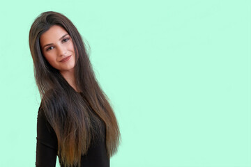 Studio waist up portrait of a tanned beautiful brunette long haired young  woman posing in front of a light green background.