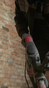 Vertical shot of black workman in hardhat and respirator demolishing cement floor with jackhammer on construction site