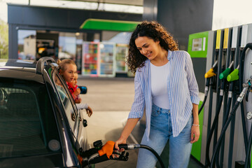 Smiling mother refueling her family car at a gas station, while her two children patiently wait...