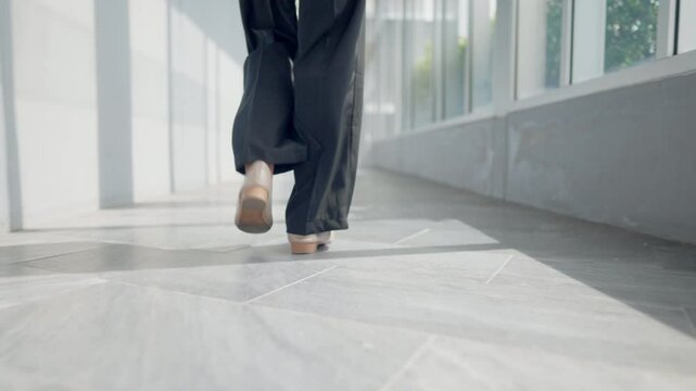 A person is walking in a hallway with their feet on the ground. The person is wearing black pants and a black shirt