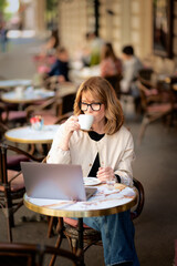 Mid aged businesswoman sitting at outdoor cafe and working on her laptop