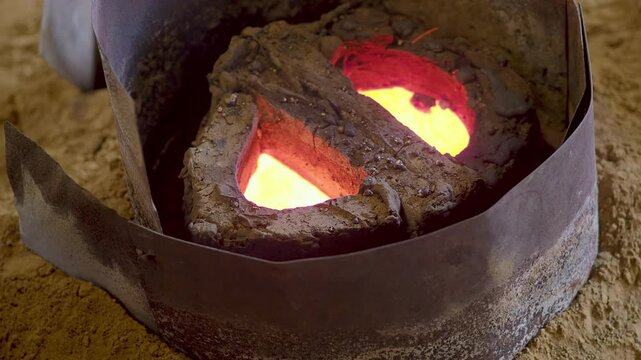Close-up shows molten alloy glowing inside a refractory mold during casting at a bell manufacturing facility, highlighting heat and artisanal technique in a traditional factory setting, slow motion