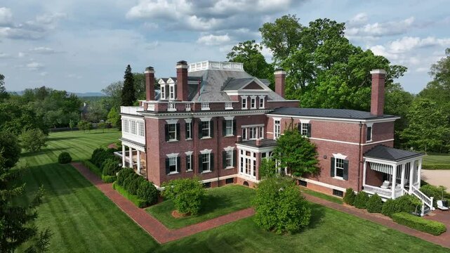 Majestic American mansion with classic brick facade and multiple chimneys, nestled in lush greenery. Elegant architecture with large windows and spacious lawn.Aerial view.