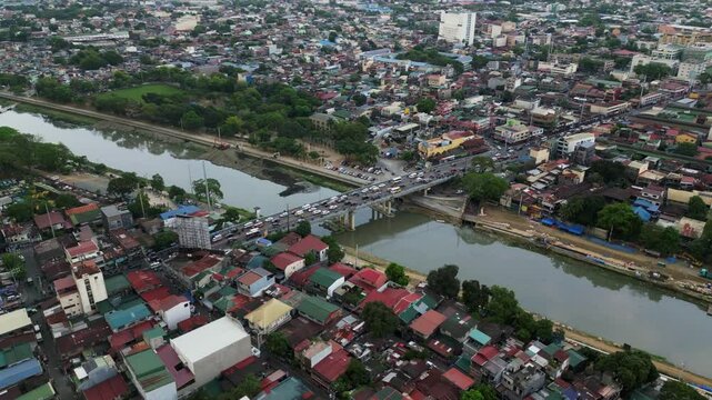 Cars cross bridge over river with dense city housing on both sides in Marikina, Metro Manila, Philippines at rush hour