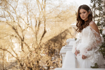 Young brunette bride in traditional long dress posing on white hotel balcony in early spring
