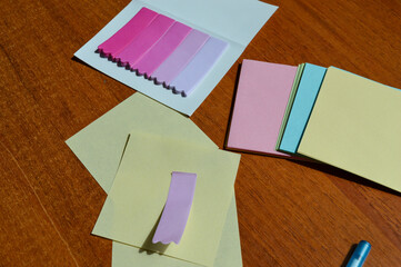 Hand writing on pastel sticky note with blue pen, surrounded by colorful paper notes and bookmarks...
