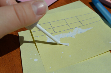 Hand applying correction fluid to paper table on sticky note. Office supplies, error correction,...